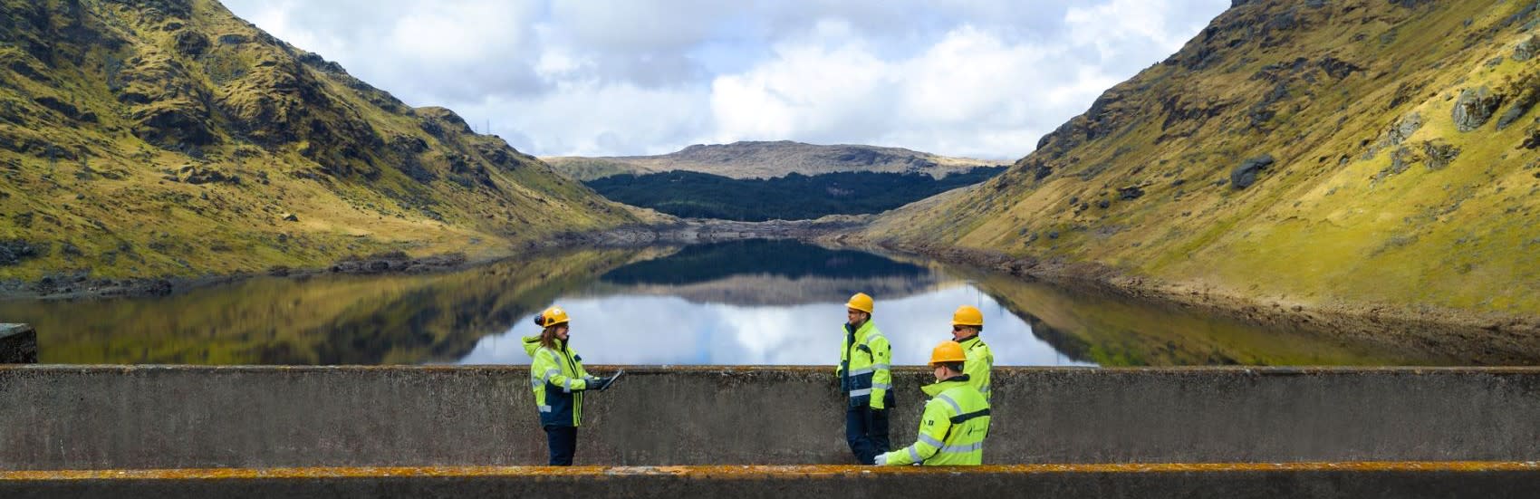 An image of SSE workers atop a dam, flanked by verdant hills and a lake in the background