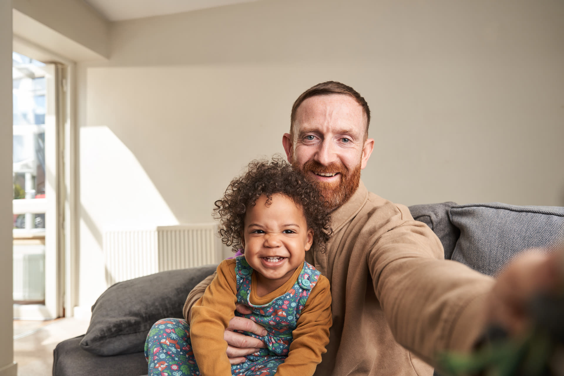 Dad and child on couch, looking directly into camera at home and smiling