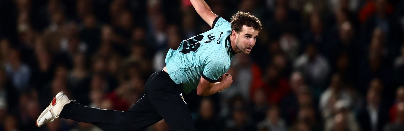 A Surrey cricketer in his kit, bowling a ball mid-action.