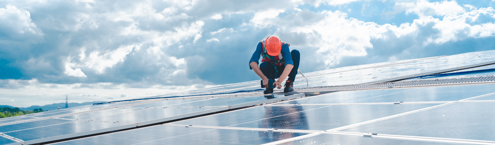 A solar technician, on top of a raft of solar panels, wearing safety gear.