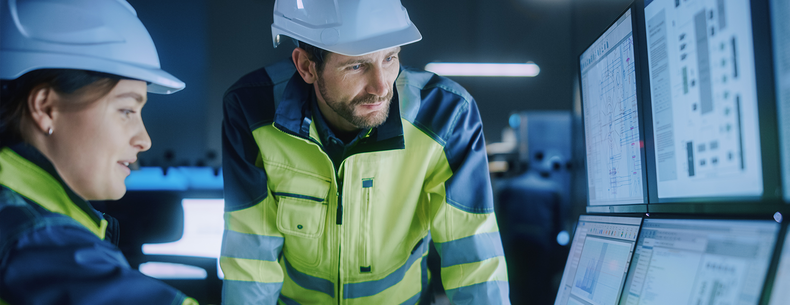 A man in high-viz and safety gear, examining a device on a wall.