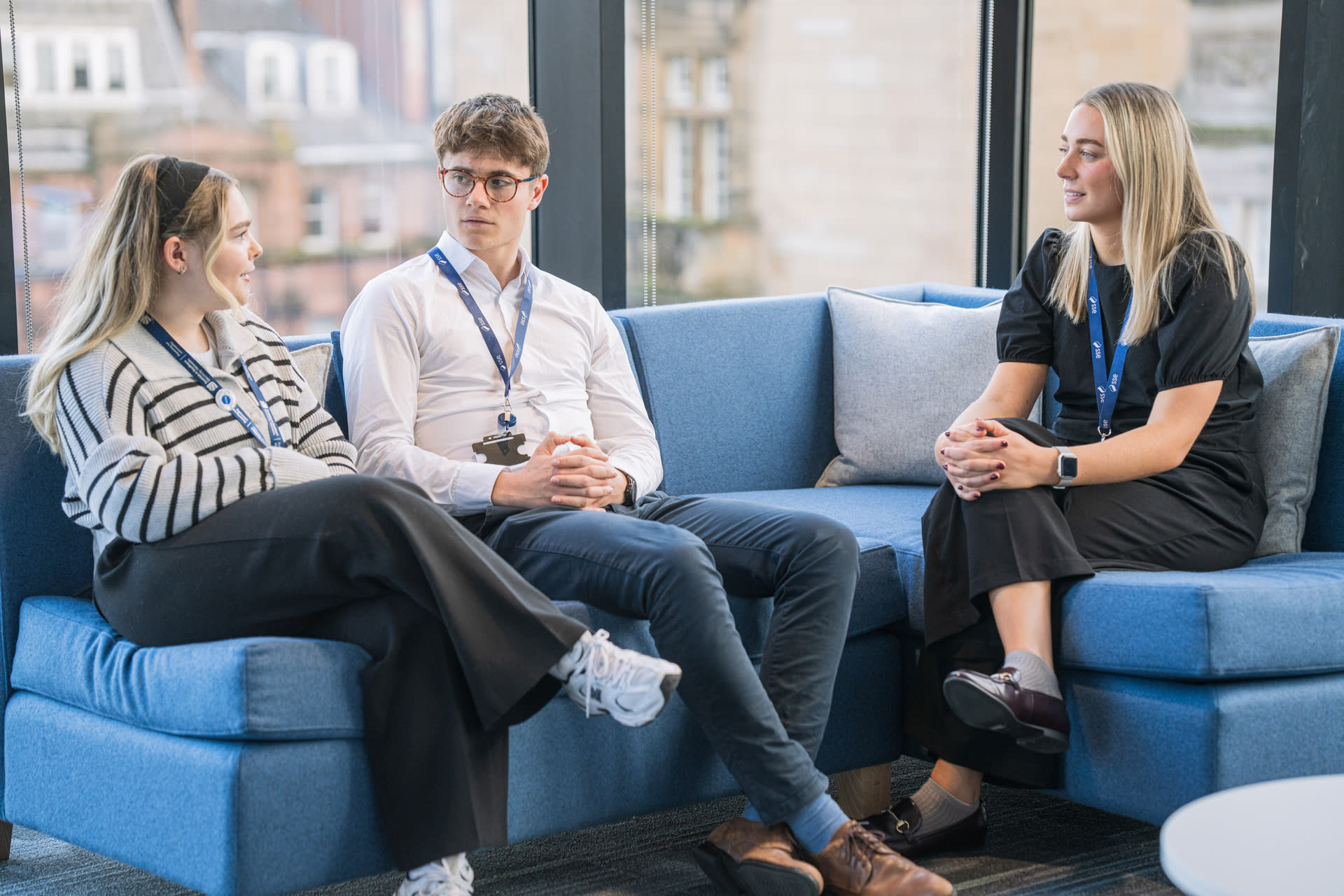 Three people sitting on a corner couch in office wear, discussing an issue.