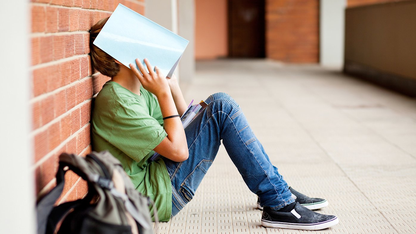 Tired or stressed child sitting in a hallway with a book over his face
