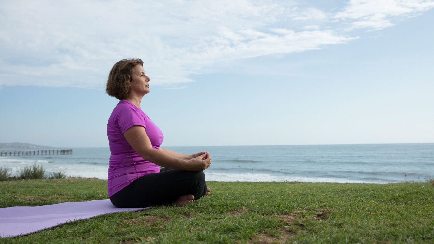 Woman meditating on yoga mat at La Jolla Shores.