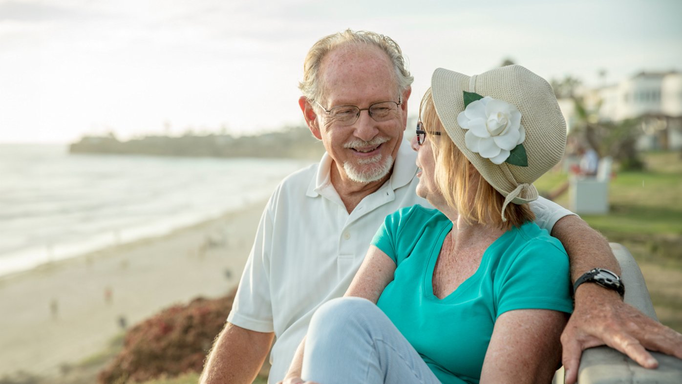 Happy senior couple sitting on bench at the beach in San Diego.