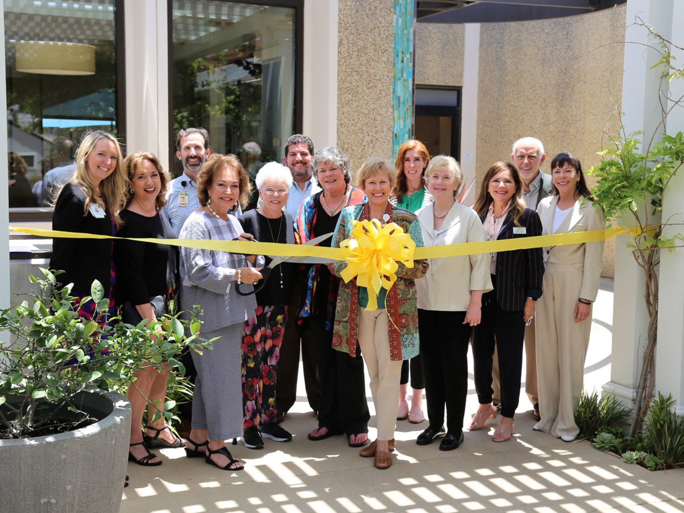 Thirteen people at ribbon cutting event standing behind yellow ribbon