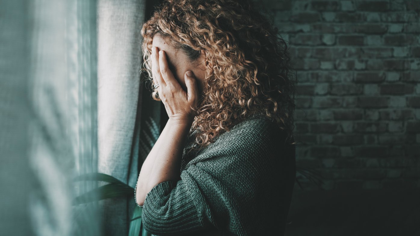 Woman holding her hands over her face while looking out the window