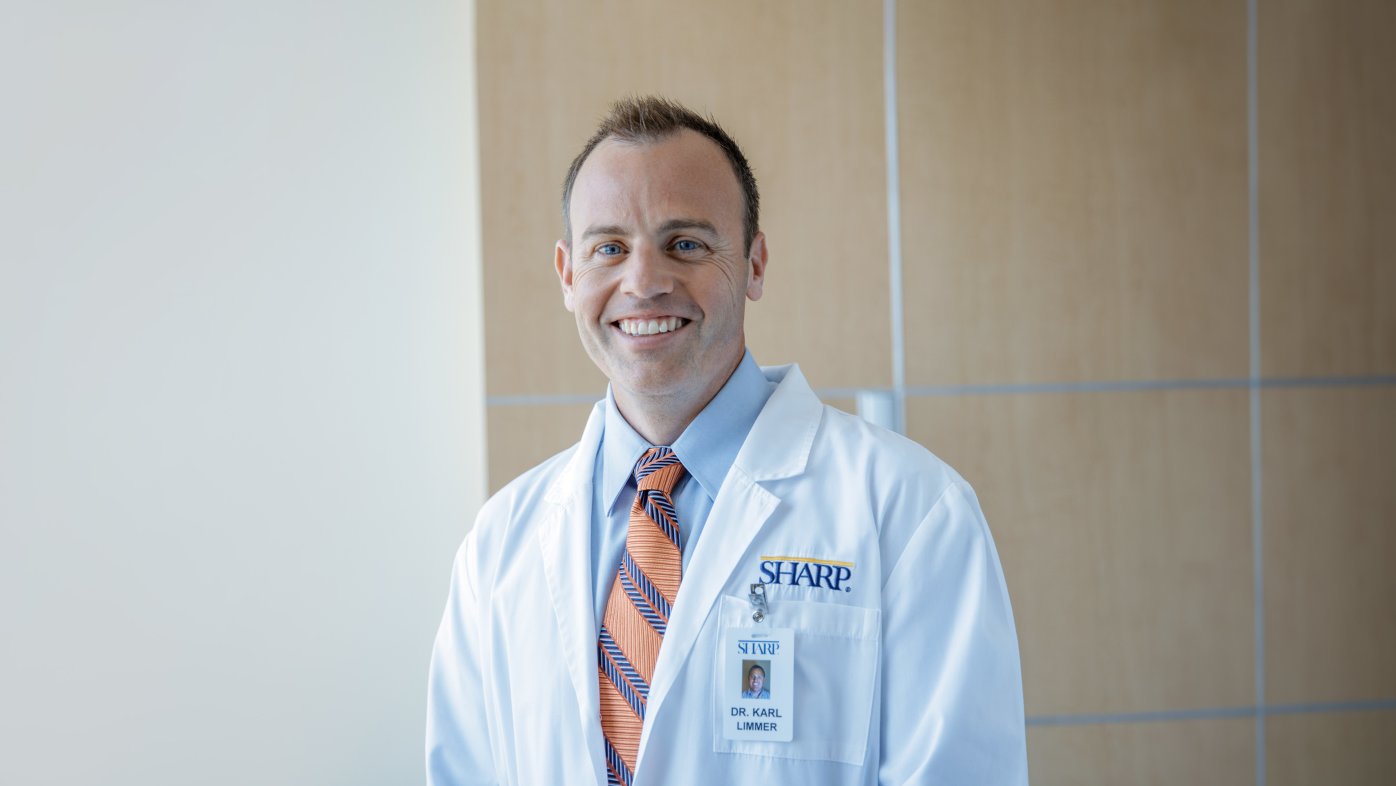 Dr. Limmer smiling in white coat and orange/blue striped tie. 