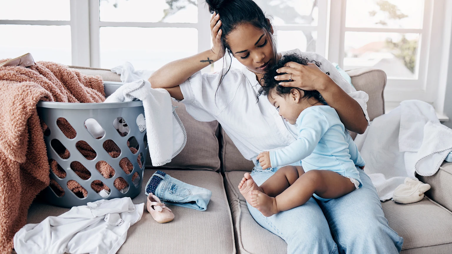 Mother comforting her baby on the couch with laundry