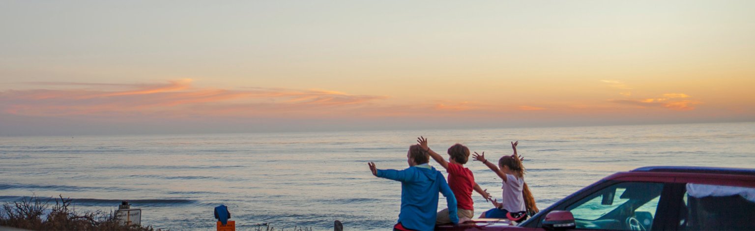 Family of four waving their hands in the air sitting on a car.