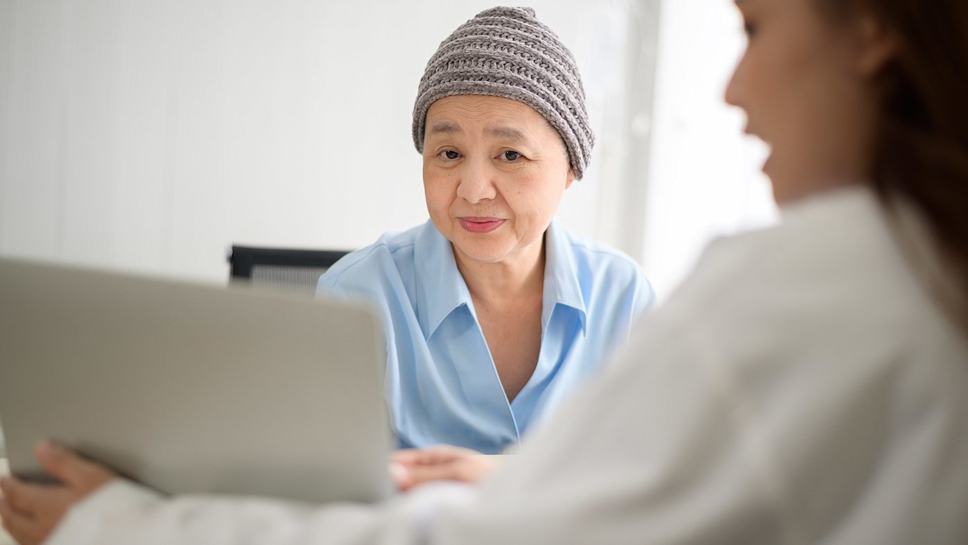 Patient wearing hat talking to her doctor holding a laptop computer