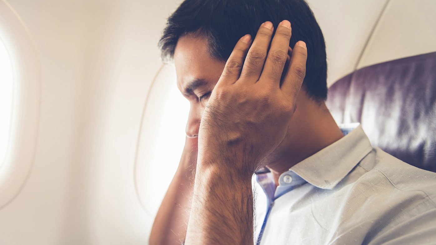 Man on airplane holding his ears in pain