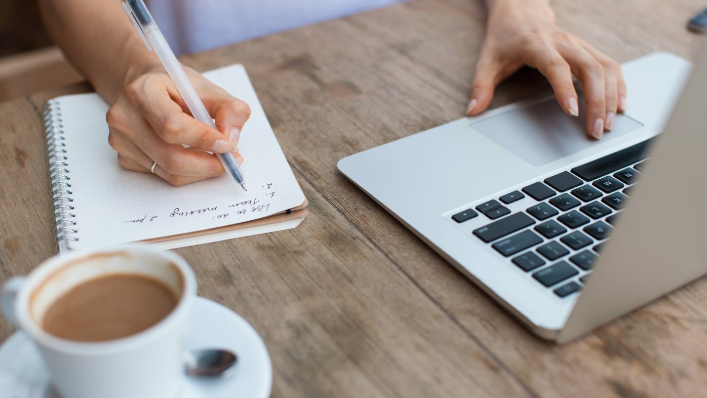 Person using laptop while writing a list in a notepad