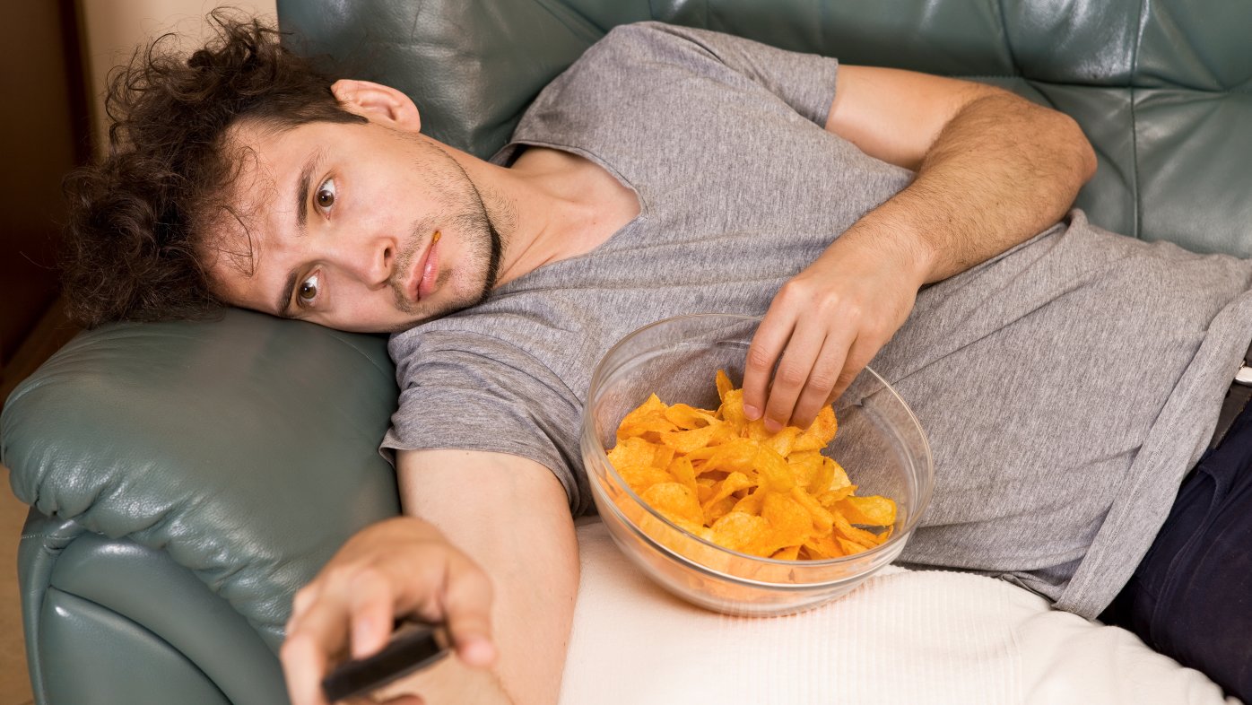 Man eating chips on couch while watching tv