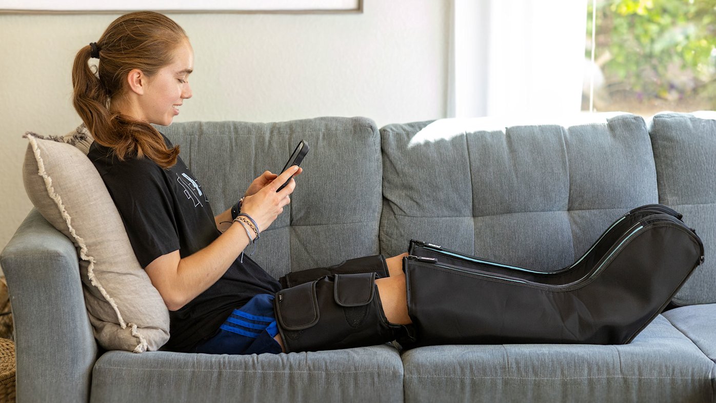 Woman on couch wearing compression boots and looking at her phone