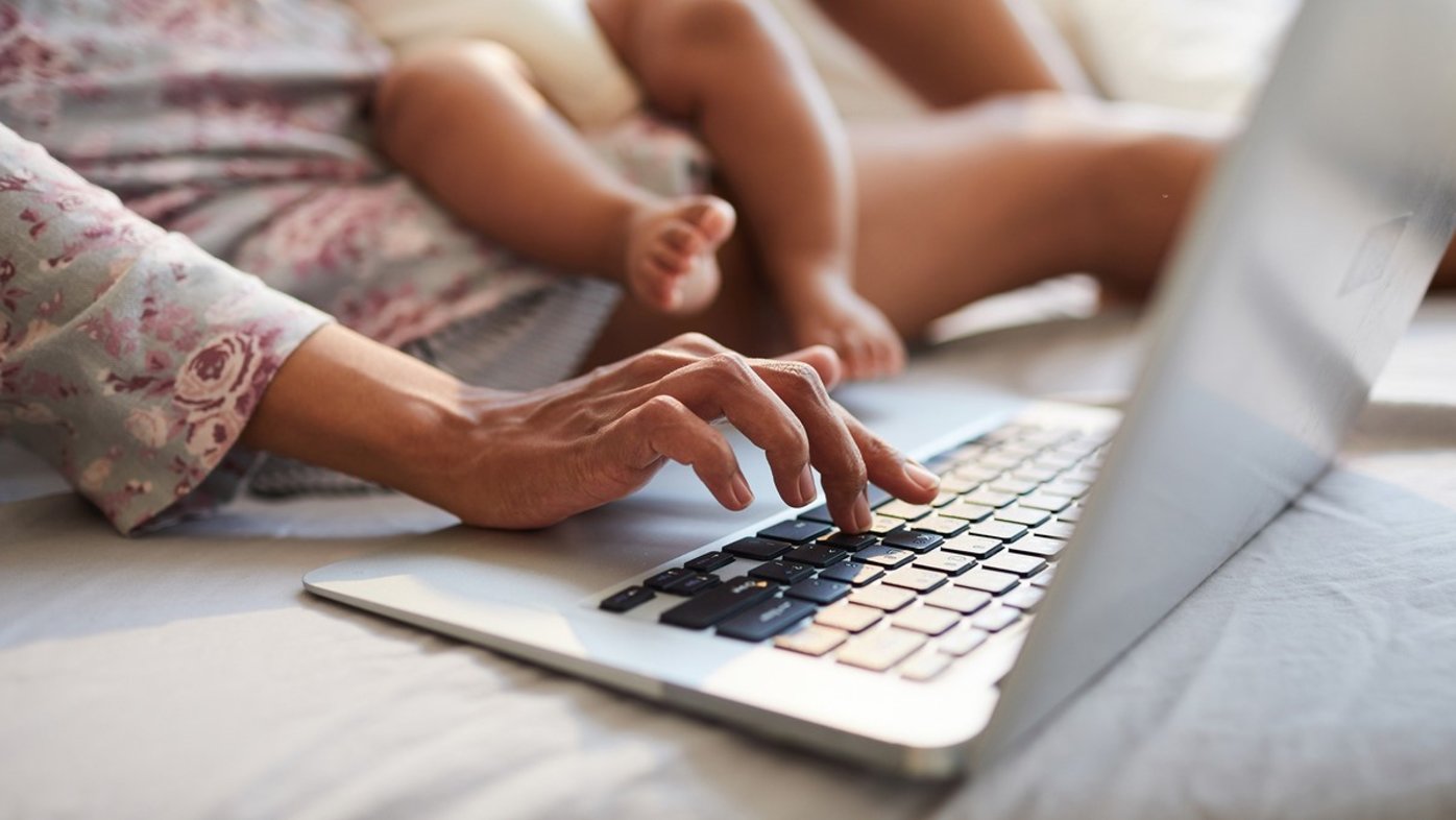 Woman typing on laptop while holding baby