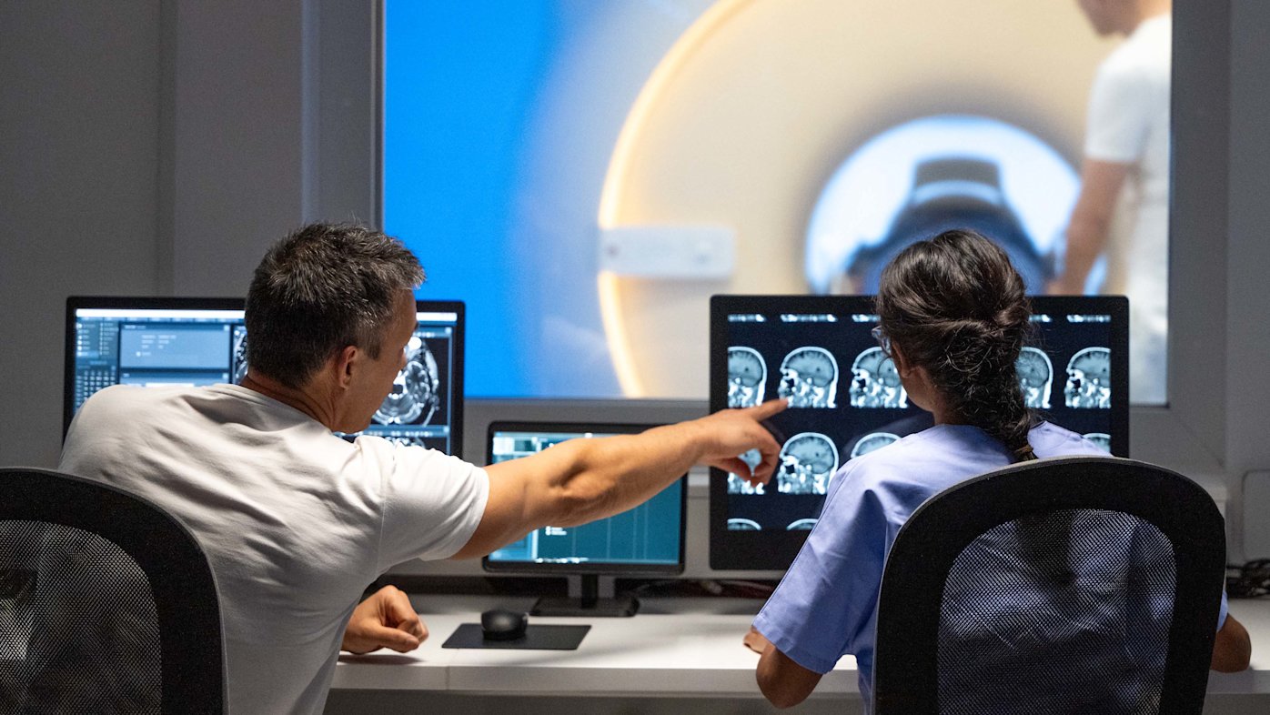 Two MRI radiologists sitting in the control room and operating the MRI scanner.