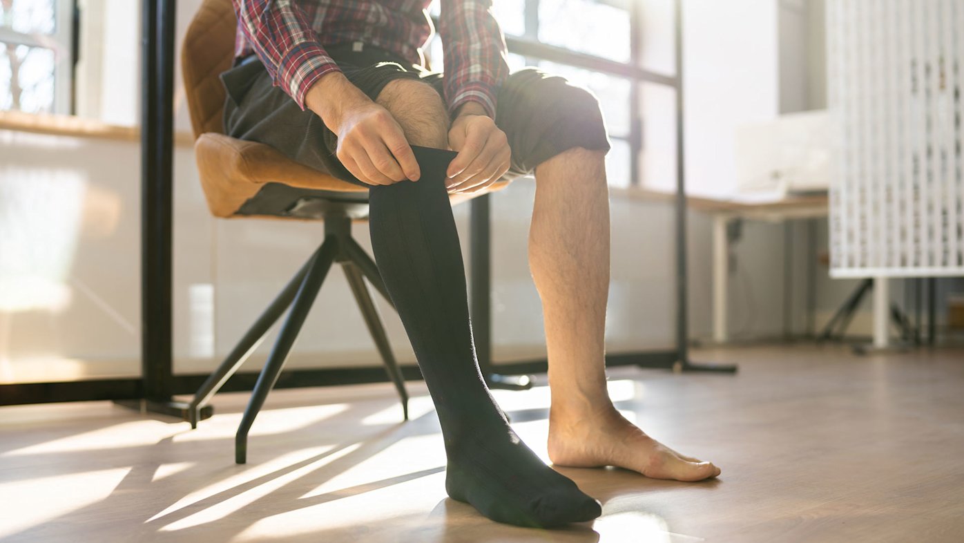 Man sitting in a chair putting on a black compression sock