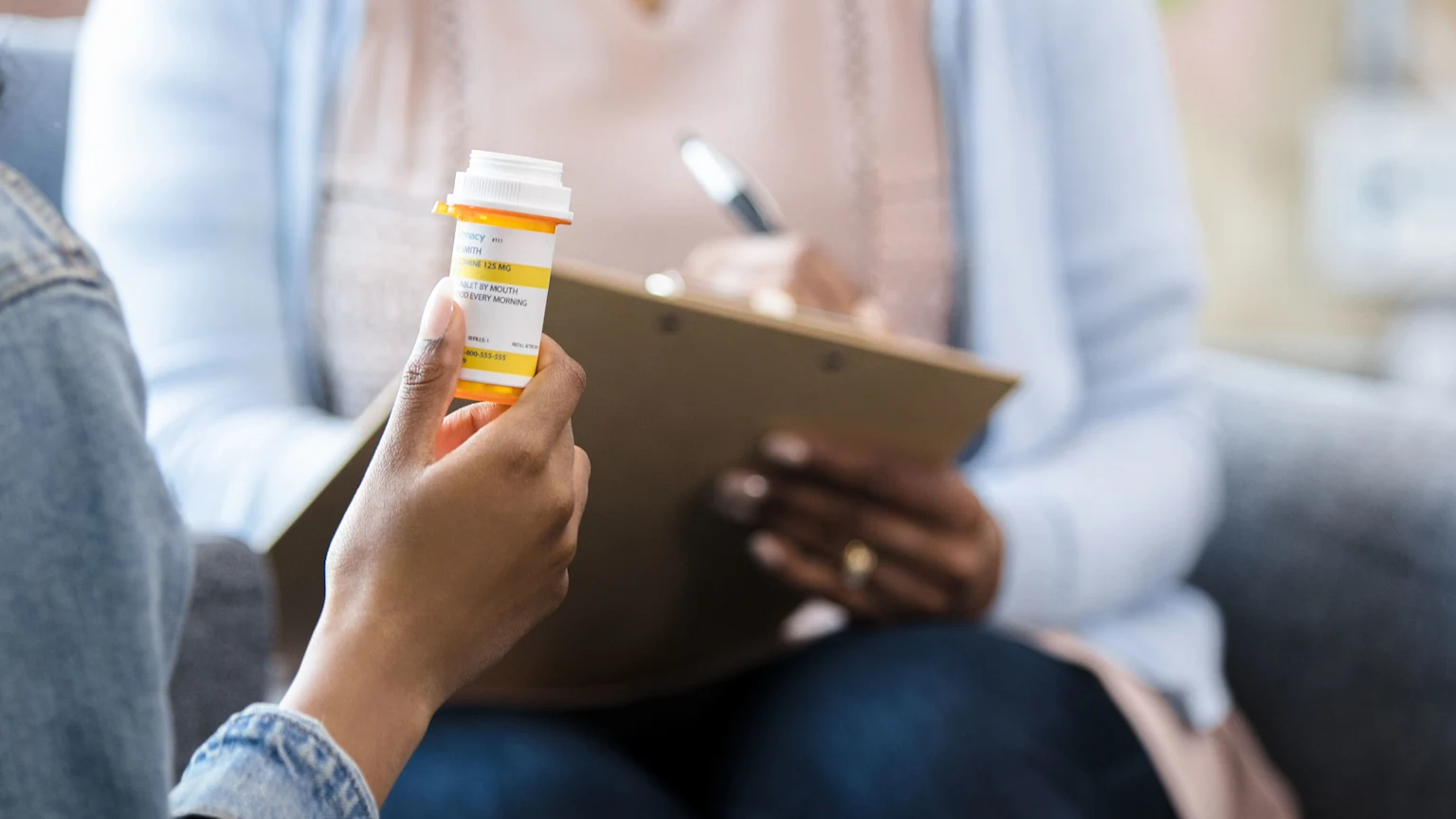 UX0904-woman-holding-medication-bottle-talking-to-therapist-duplex-3840x2160