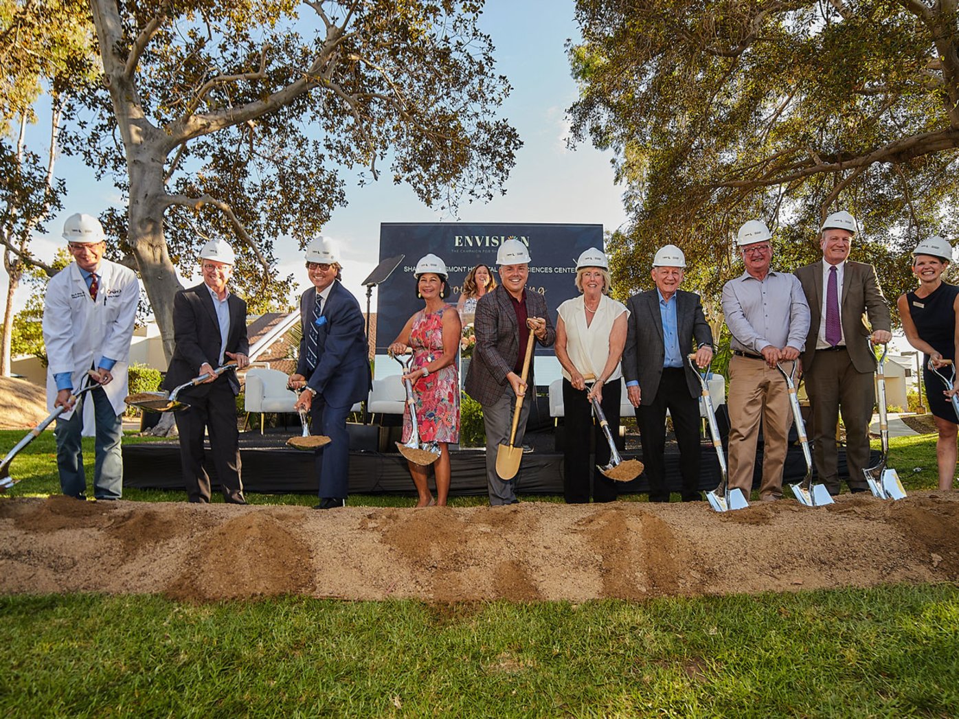 Ten people in hard hats with shovels during event groundbreaking.