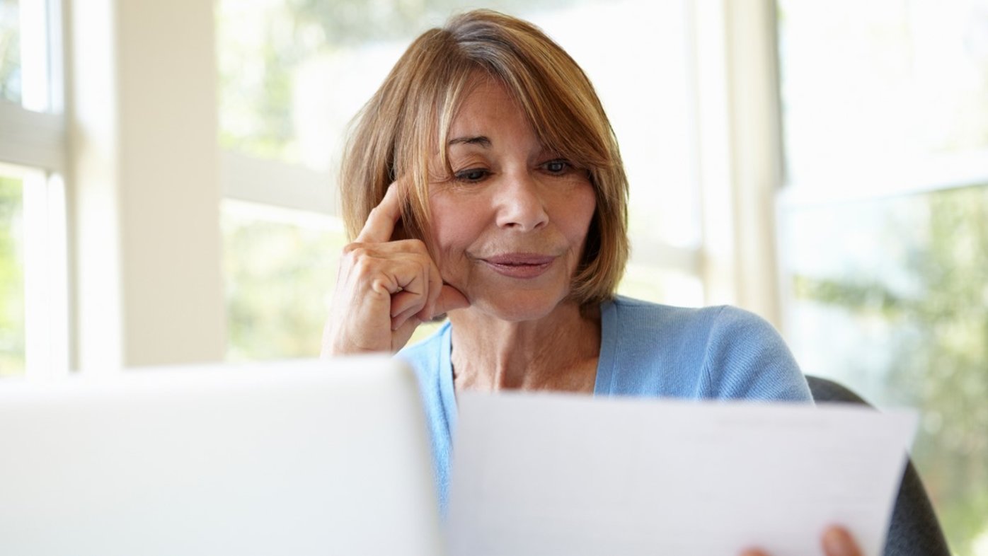 Woman reading paperwork with a laptop computer