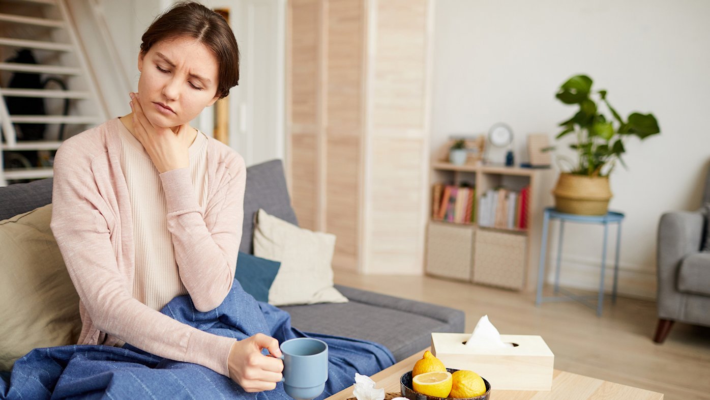 Sick woman holding her sore throat and a cup of tea