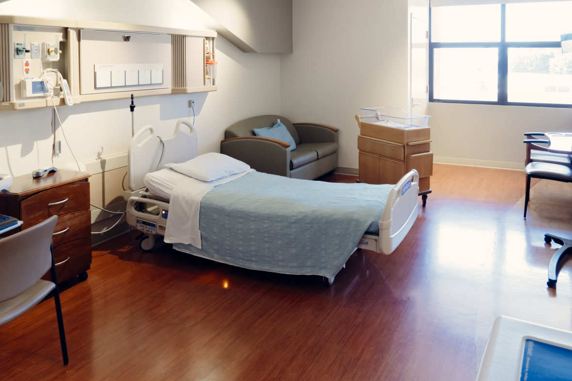 Hospital room with hospital bed, green couch, wooden floors and windows