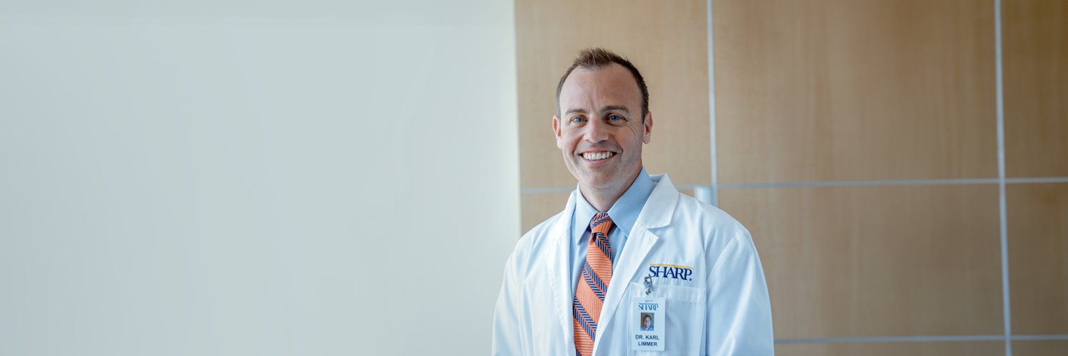 Dr. Limmer smiling in white coat and orange/blue striped tie. 