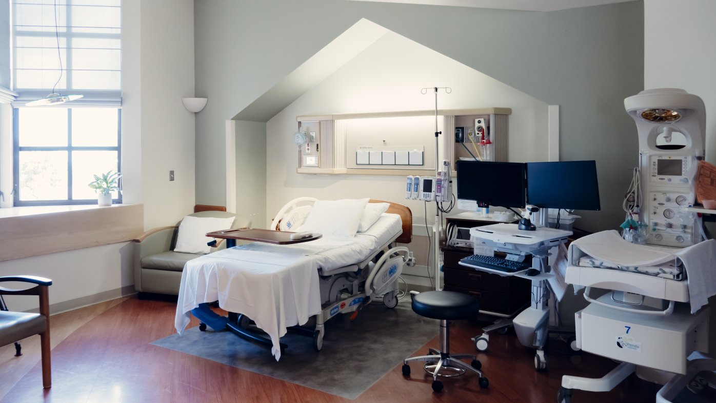 Room with windows, wooden floors, hospital bed, computer and machine to monitor baby