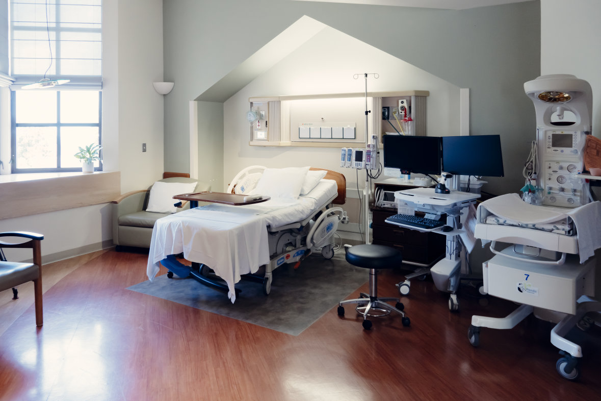 Room with windows, wooden floors, hospital bed, computer and machine to monitor baby