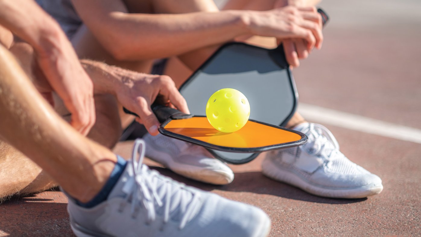 Person holding a pickleball on top of a pickleball paddle
