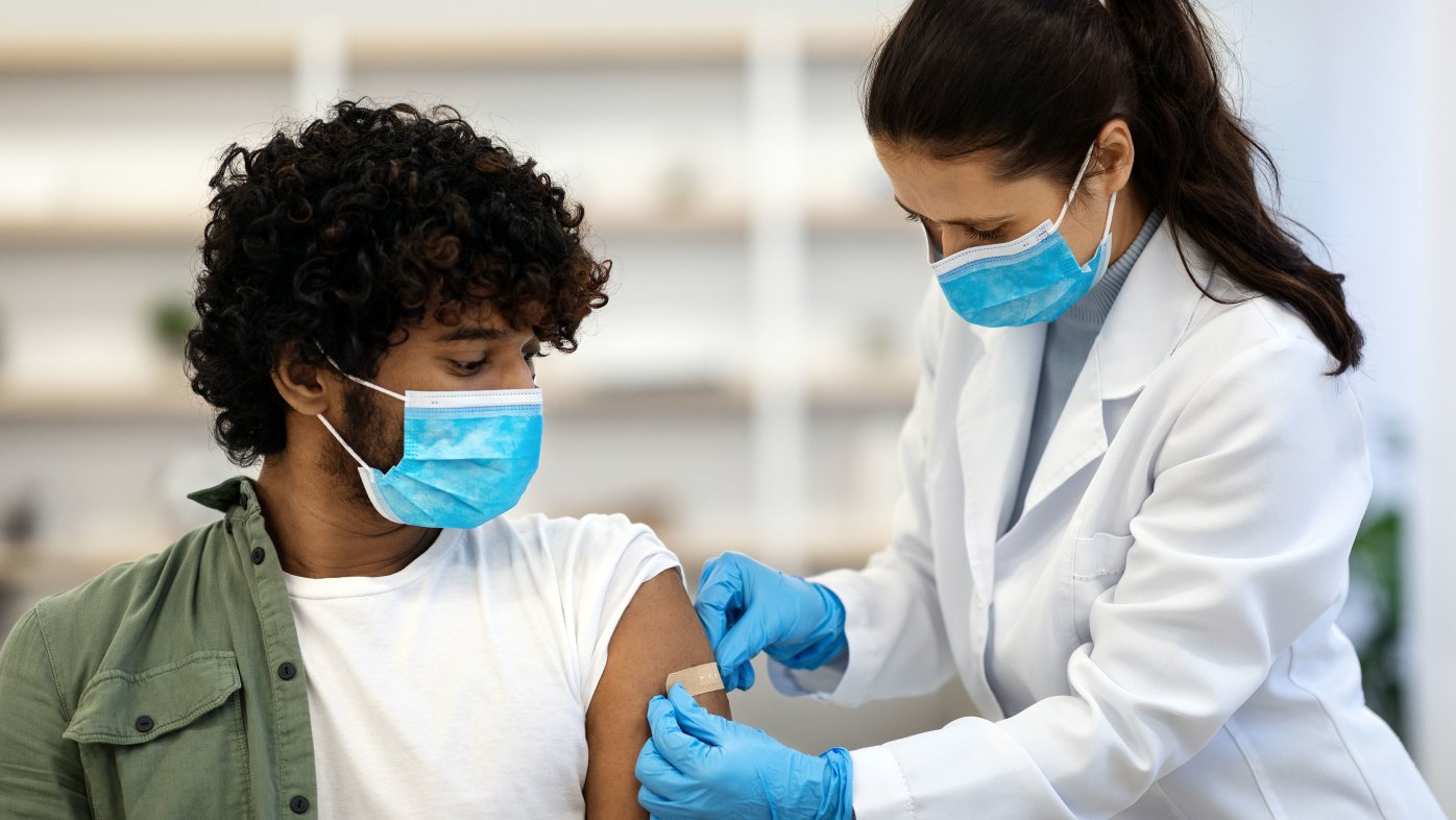 Masked health professional applying bandage on patient's arm, after getting vaccinated.