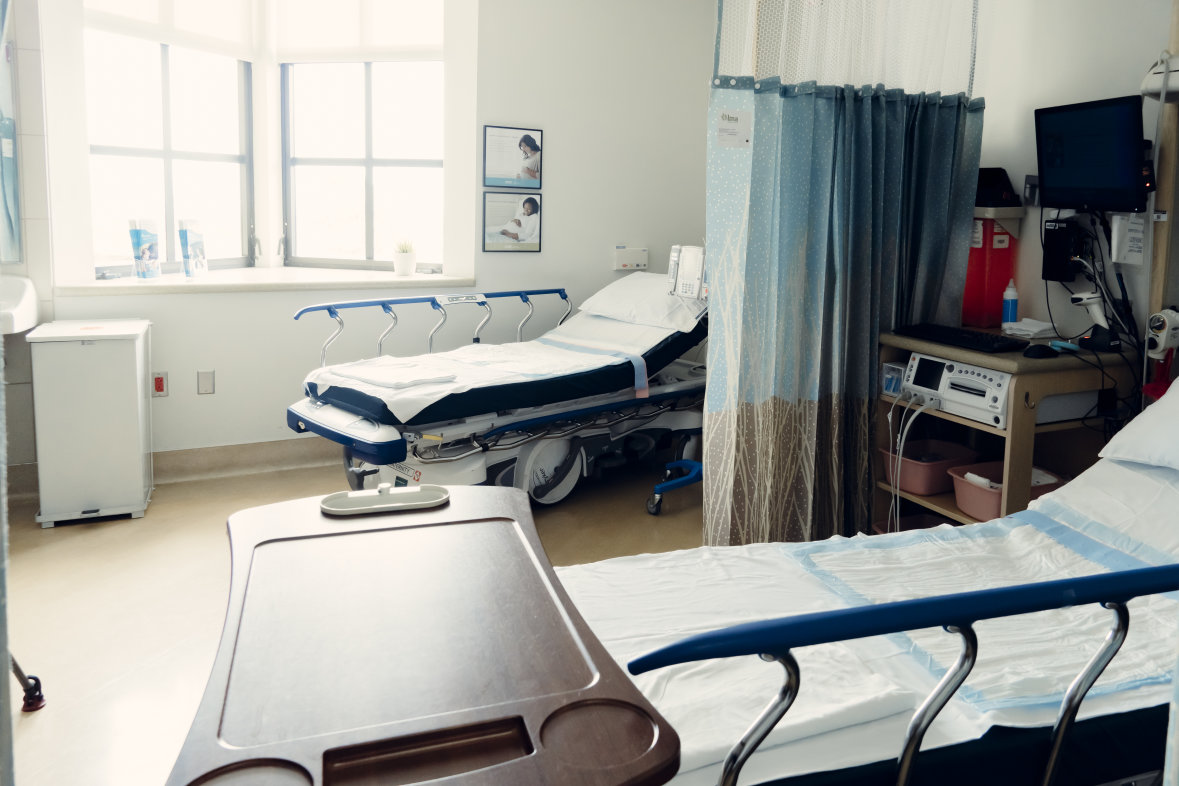 Hospital room with two beds and curtain in between and windows in the background.