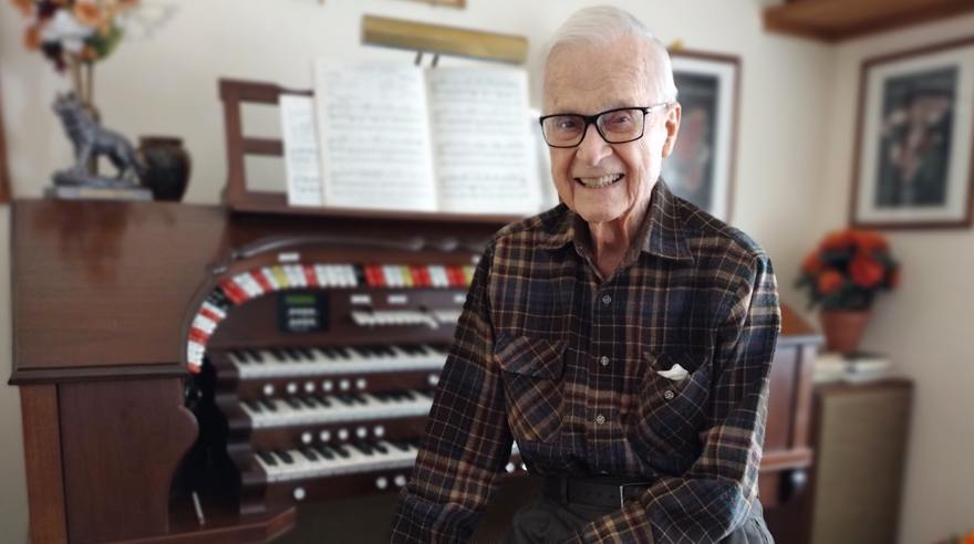 Mr. John “Jack” Seaman poses in front of an organ he plays at home.