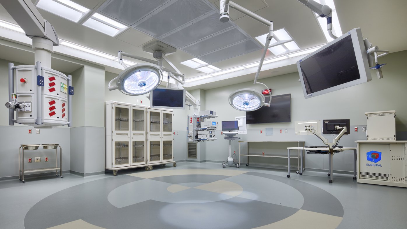 Operating room with gray and beige floors with screen, equipment and lights attached to ceiling