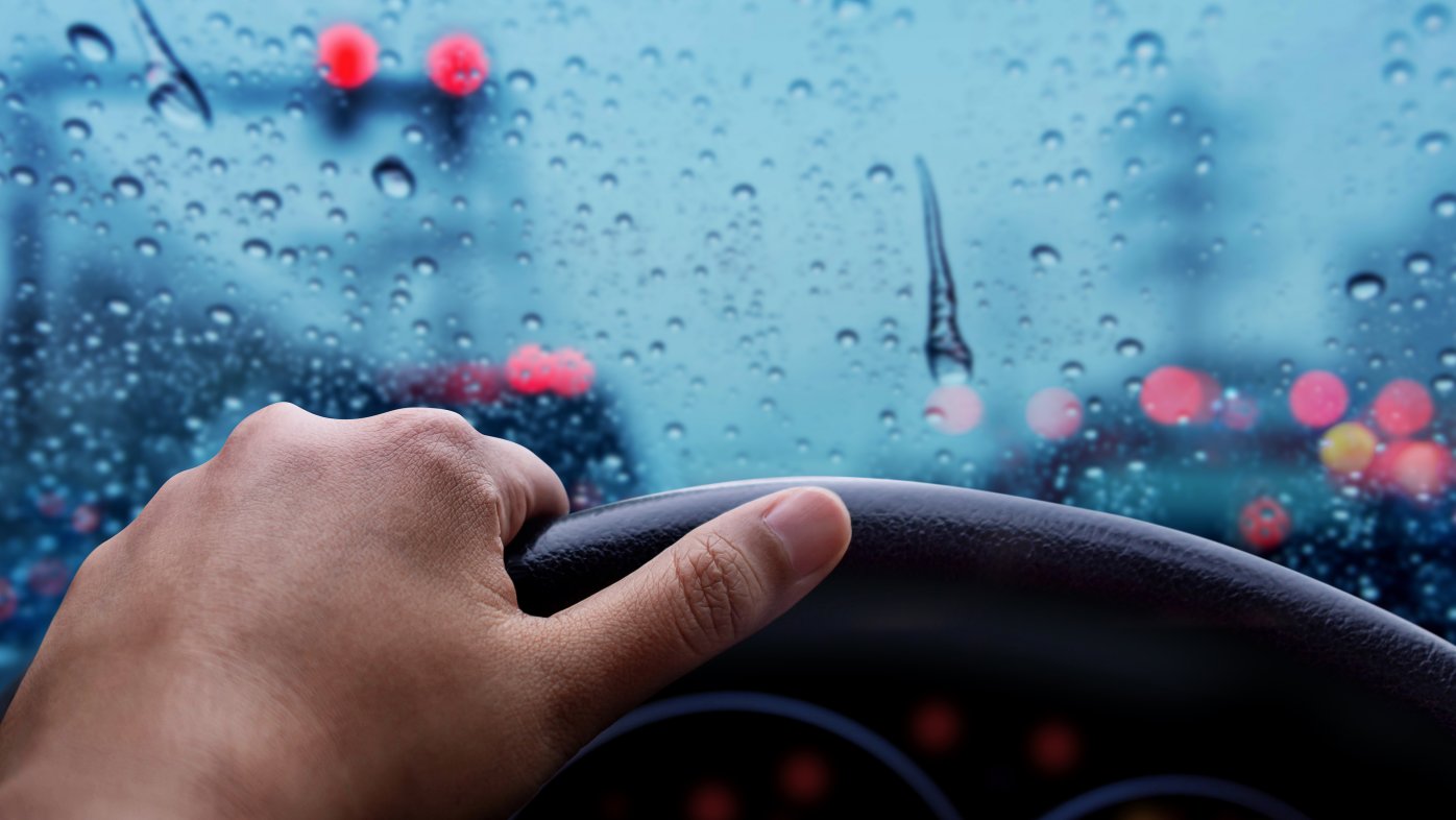 Hand on steering wheel of car driving in the rain