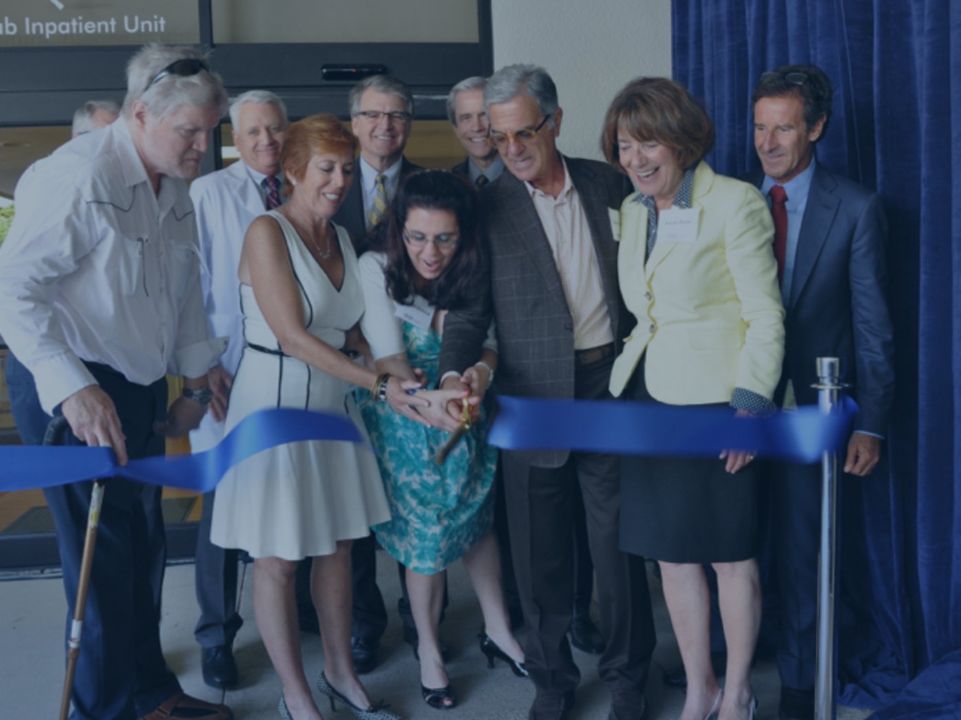Nine people at ribbon cutting with two women cutting blue ribbon with scissors