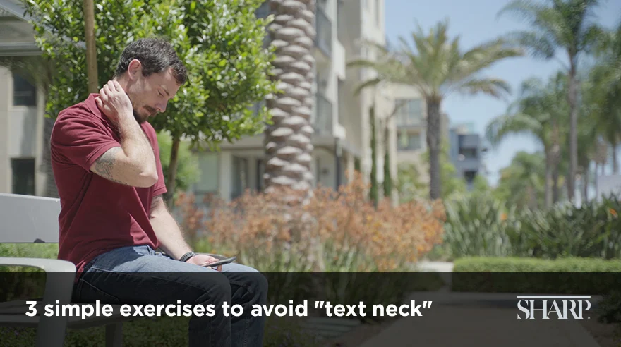 Hombre sentado al aire libre sosteniéndose el cuello mientras mira el teléfono móvil