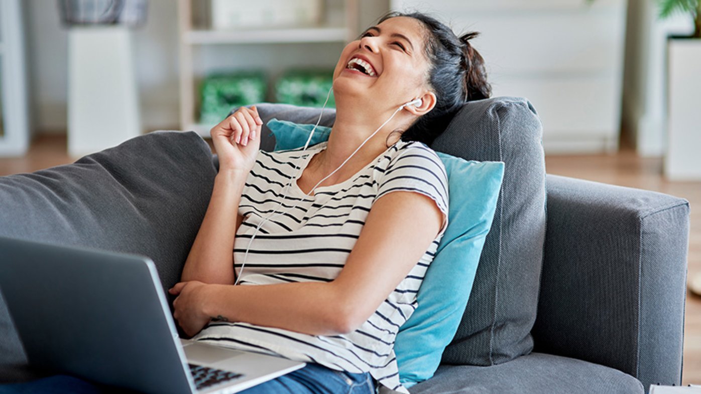 Woman laughing during a video conversation laying on couch