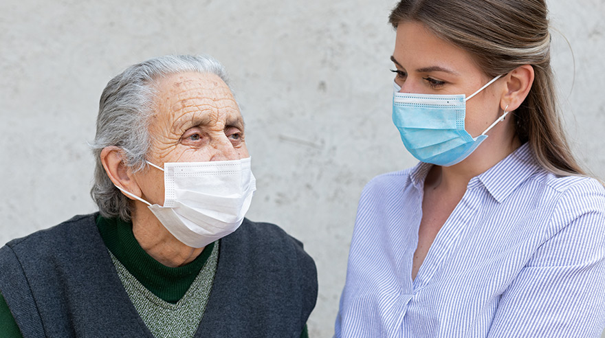 Caregiver works with elderly ill woman wearing mask because of COVID-19