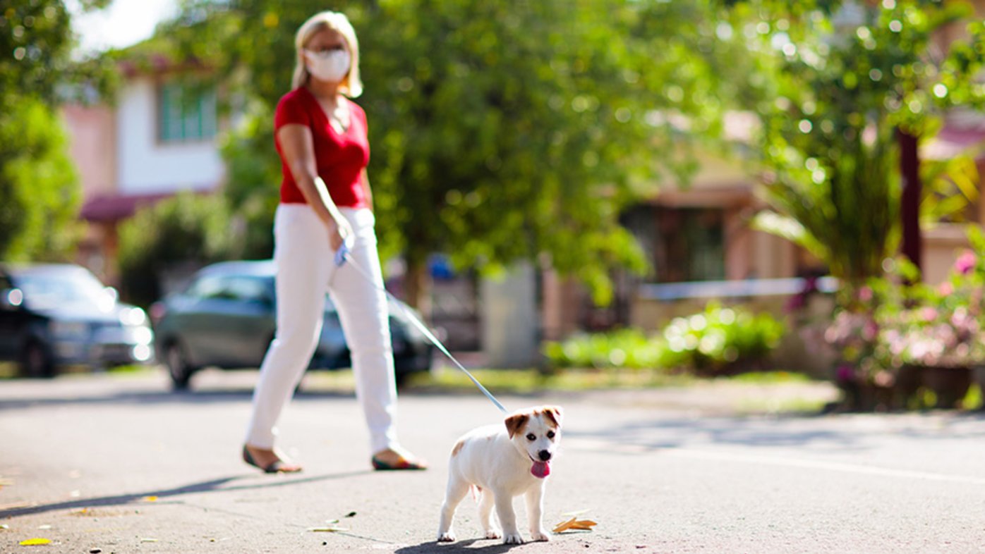 Woman with mask walking her dog on a leash