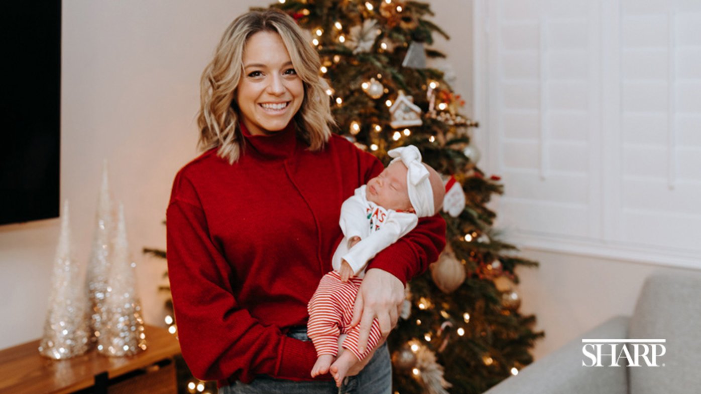 Woman holding infant in front of Christmas tree