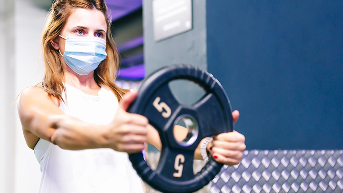 Woman lifting weights at a gym with a mask on.