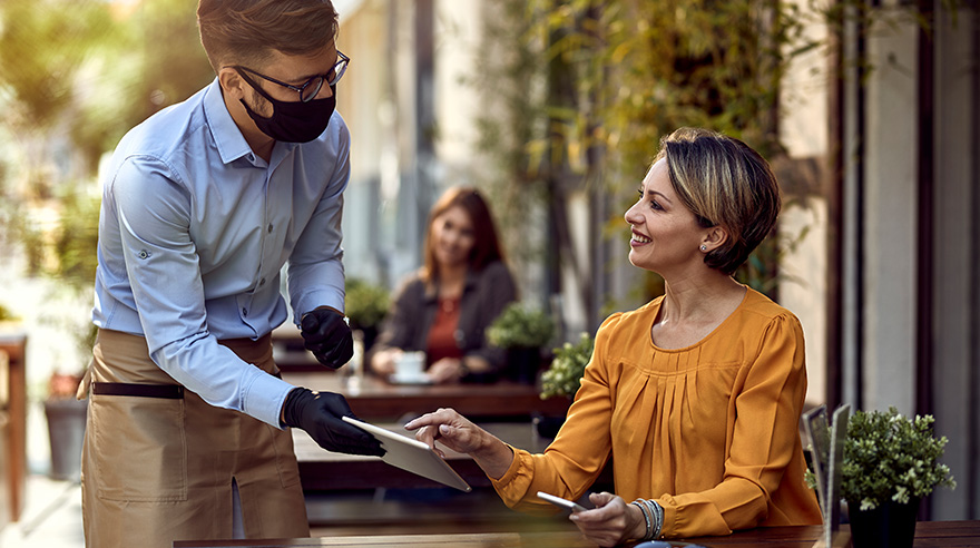 Woman talking to a waiter who is wearing protective mask.