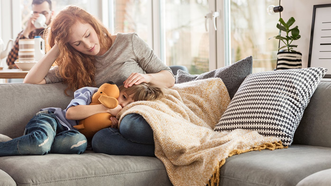 Mother taking care of a sleepy child while sitting on a couch in the living room.