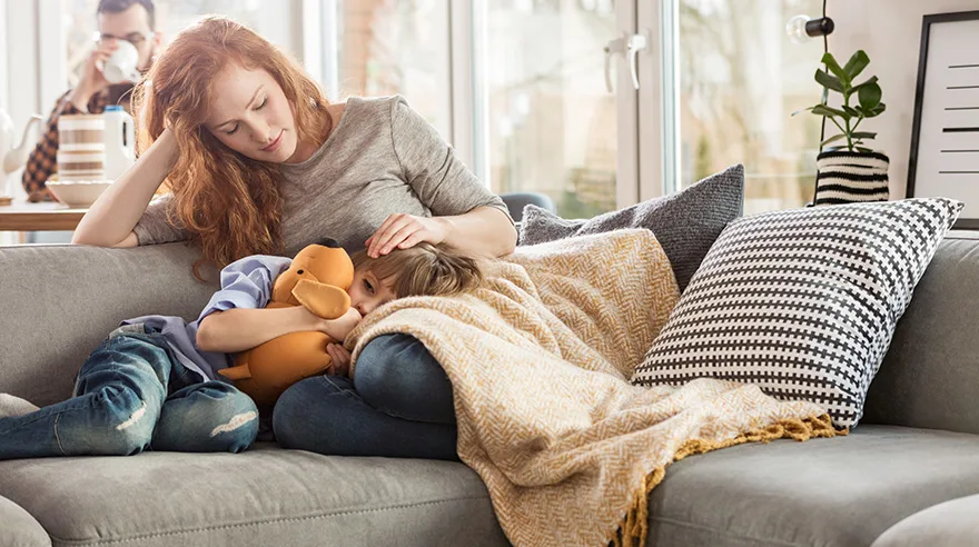 Mother taking care of a sleepy child while sitting on a couch in the living room.