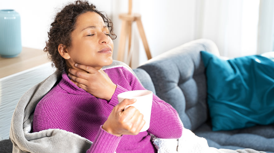 Woman holding her sore throat and holding a tea cup