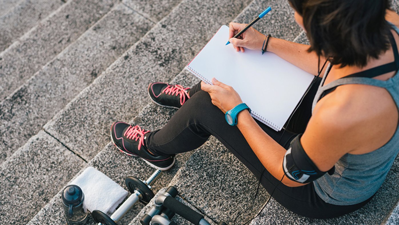 Woman writing goals in notepad while exercising