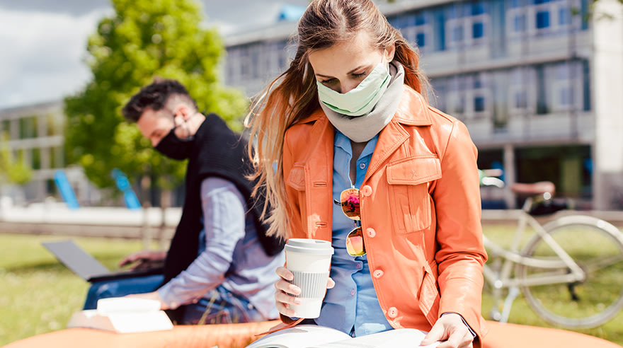 Two college students study on campus wearing masks