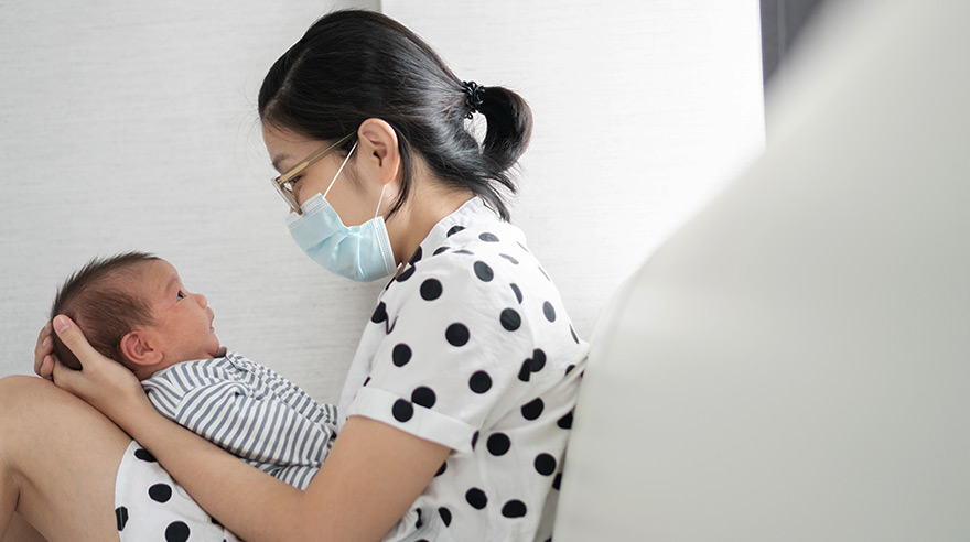 Mother wearing face mask and holding newborn baby